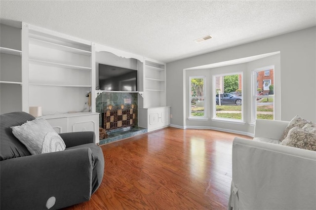 living room with a textured ceiling, wood finished floors, built in shelves, and baseboards