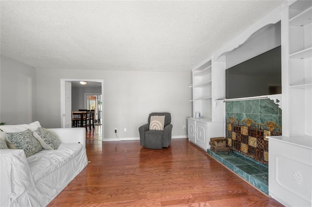 living area featuring a textured ceiling, wood finished floors, a tiled fireplace, and built in features