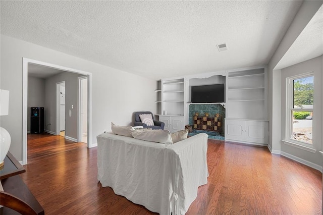 living area with wood finished floors, a textured ceiling, baseboards, and a tile fireplace