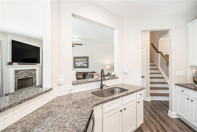 kitchen featuring sink, dark wood-type flooring, white cabinets, stone countertops, and a stone fireplace