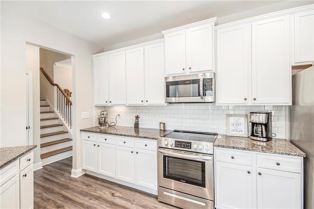 kitchen featuring hardwood / wood-style flooring, appliances with stainless steel finishes, white cabinets, stone countertops, and decorative backsplash