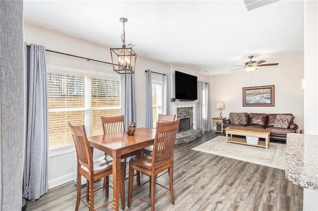 dining space with ceiling fan with notable chandelier, a stone fireplace, and hardwood / wood-style floors