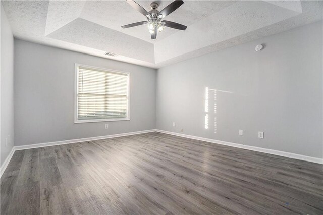 empty room featuring ceiling fan, dark wood-type flooring, a raised ceiling, and a textured ceiling