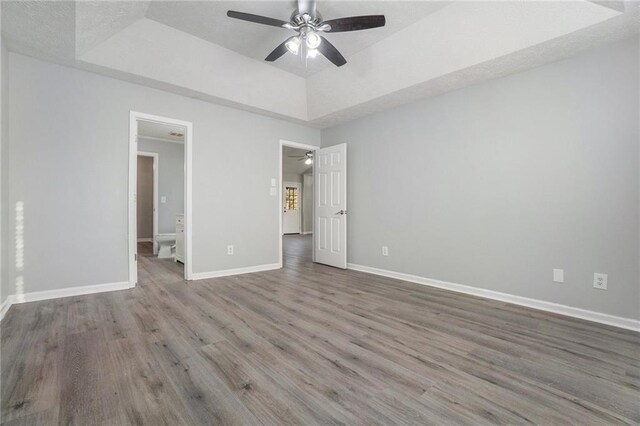 unfurnished bedroom with ceiling fan, a tray ceiling, and hardwood / wood-style floors