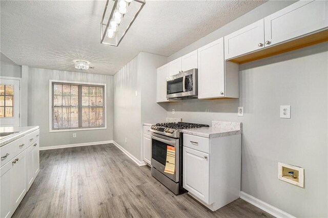 kitchen featuring appliances with stainless steel finishes, a textured ceiling, white cabinets, and light hardwood / wood-style floors