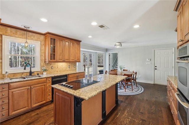 kitchen with black electric stovetop, brown cabinetry, a sink, and visible vents