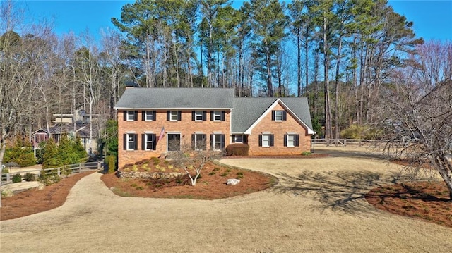 colonial-style house with dirt driveway and fence