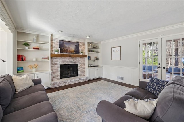 living area with visible vents, dark wood finished floors, a textured ceiling, a brick fireplace, and built in shelves