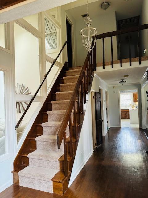 staircase featuring hardwood / wood-style floors, ornamental molding, and a notable chandelier