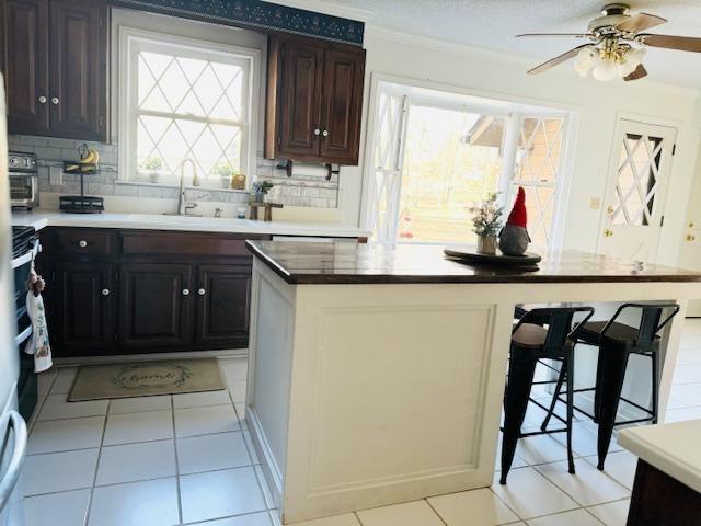 kitchen featuring sink, ceiling fan, tasteful backsplash, light tile patterned flooring, and dark brown cabinetry