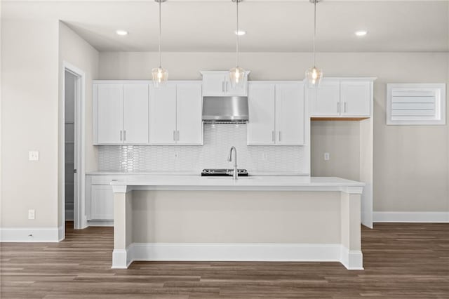 kitchen featuring white cabinets, range hood, pendant lighting, and a kitchen island with sink