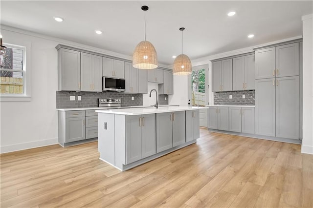 kitchen with light wood finished floors, gray cabinets, stainless steel appliances, and light countertops