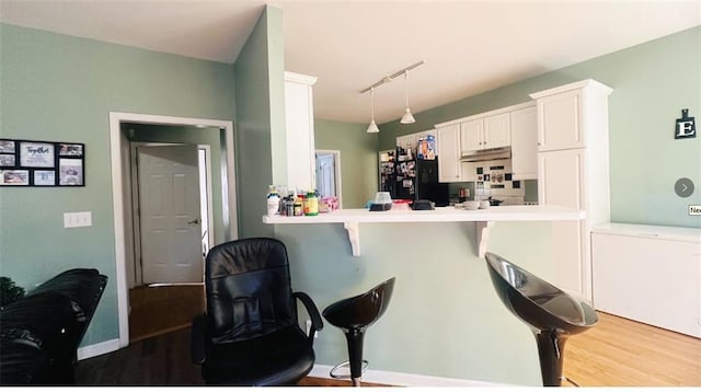 kitchen with rail lighting, freestanding refrigerator, white cabinets, wood finished floors, and a kitchen bar