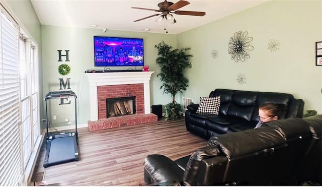 living area with a brick fireplace, baseboards, a ceiling fan, and wood finished floors