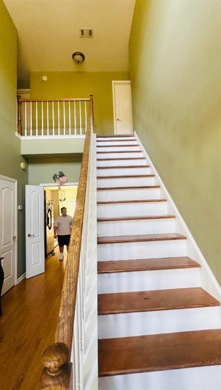 staircase with a towering ceiling, wood finished floors, and visible vents