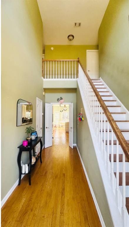 hallway with stairs, a high ceiling, wood finished floors, and baseboards