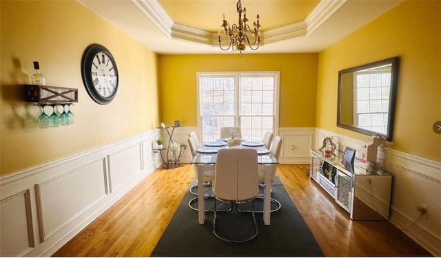 dining room with crown molding, a raised ceiling, wood finished floors, and wainscoting