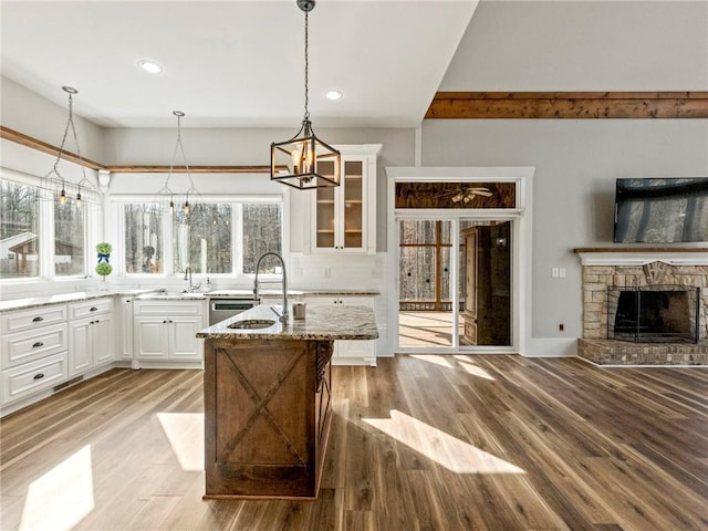 kitchen featuring light stone counters, a fireplace, light wood-style flooring, glass insert cabinets, and a sink