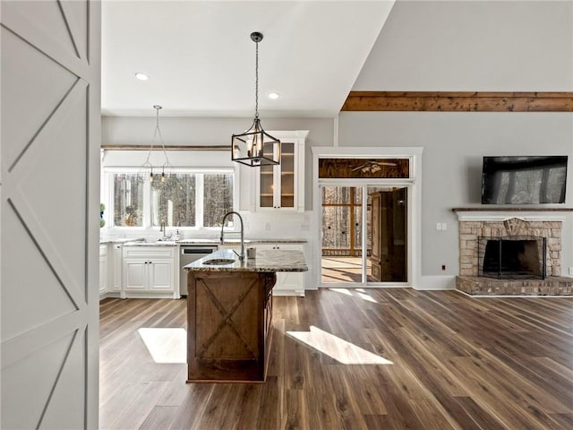 kitchen featuring a stone fireplace, light stone counters, wood finished floors, white cabinets, and glass insert cabinets