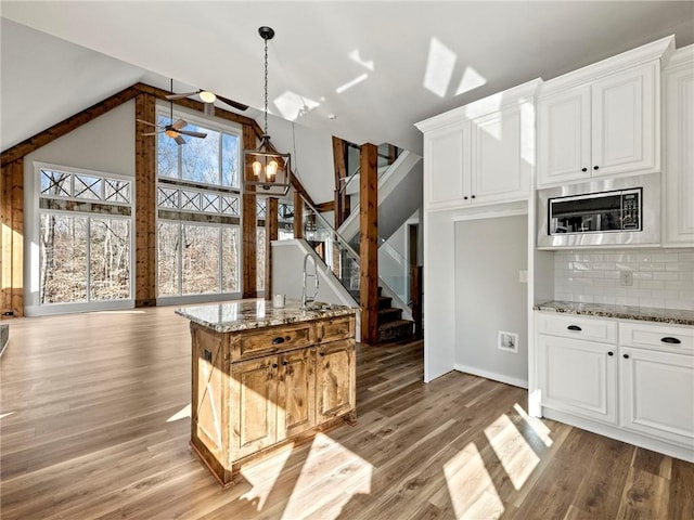 kitchen with light stone counters, light wood finished floors, tasteful backsplash, white cabinets, and built in microwave