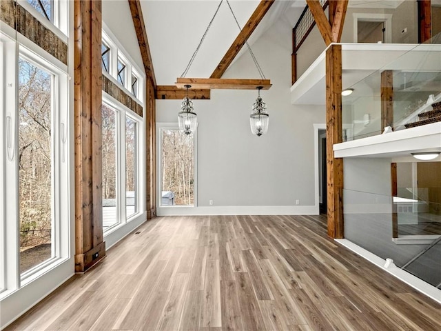 unfurnished living room with baseboards, high vaulted ceiling, wood finished floors, and beamed ceiling