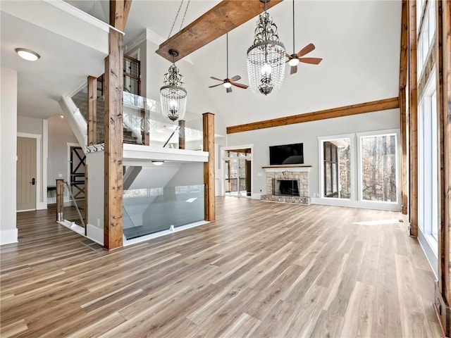 unfurnished living room with ceiling fan with notable chandelier, a fireplace, a towering ceiling, and wood finished floors