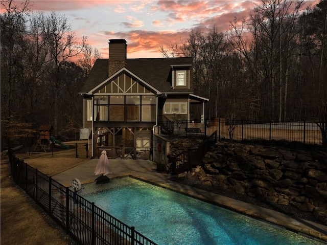 back of property at dusk featuring a fenced in pool, a patio, a chimney, and fence