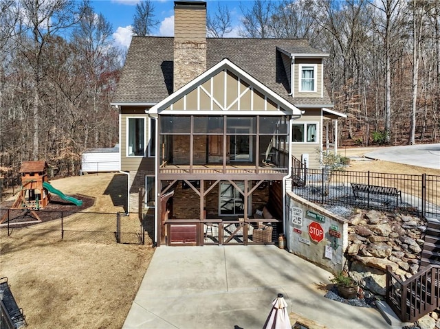 back of property with roof with shingles, a playground, a chimney, a sunroom, and fence