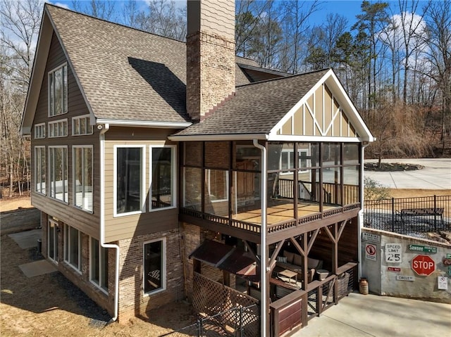 rear view of house featuring a shingled roof, a sunroom, a chimney, a wooden deck, and brick siding