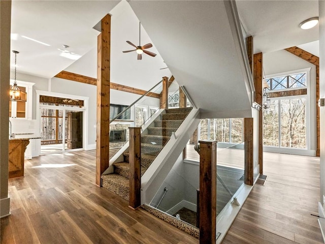 staircase with high vaulted ceiling, ceiling fan with notable chandelier, baseboards, and wood finished floors