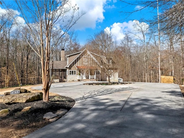 view of front of house featuring stone siding, concrete driveway, a porch, and a chimney