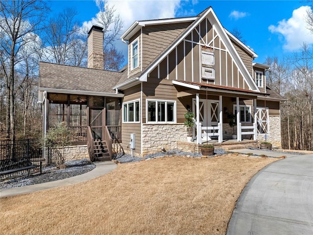 rear view of property with covered porch, a sunroom, stone siding, roof with shingles, and a chimney