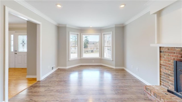 unfurnished living room featuring a brick fireplace, wood finished floors, crown molding, and a healthy amount of sunlight