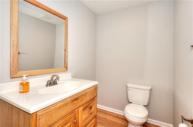 half bathroom with baseboards, toilet, wood finished floors, and vanity