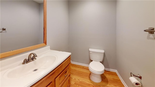 half bathroom featuring vanity, toilet, wood finished floors, and baseboards