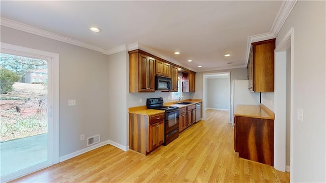 kitchen featuring black appliances, light countertops, light wood-type flooring, and a sink