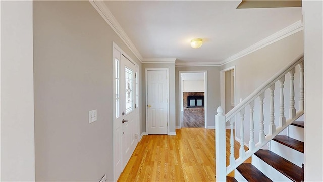 foyer with stairway, baseboards, light wood finished floors, a fireplace, and ornamental molding