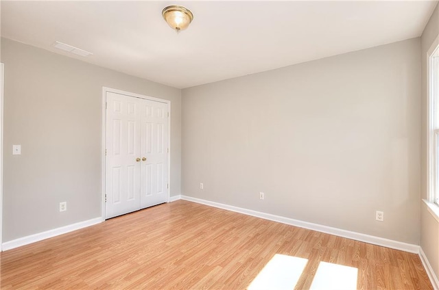 unfurnished bedroom with visible vents, light wood-style floors, baseboards, and a closet