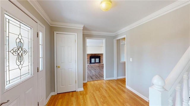 foyer featuring a fireplace, baseboards, light wood-type flooring, and ornamental molding