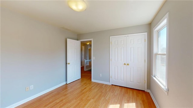 unfurnished bedroom featuring light wood-type flooring, multiple windows, baseboards, and a closet