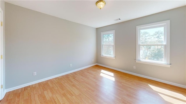 empty room with light wood-style flooring, visible vents, and baseboards