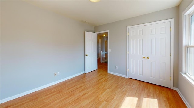 unfurnished bedroom with a closet, baseboards, multiple windows, and light wood-style flooring