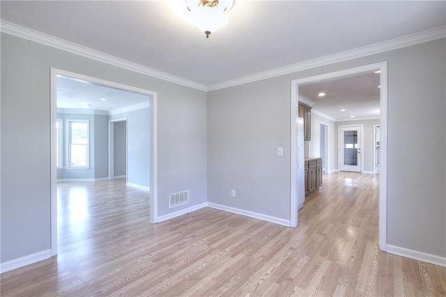 empty room with visible vents, baseboards, ornamental molding, and light wood finished floors