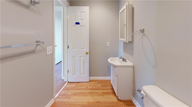 bathroom with toilet, vanity, baseboards, and wood finished floors