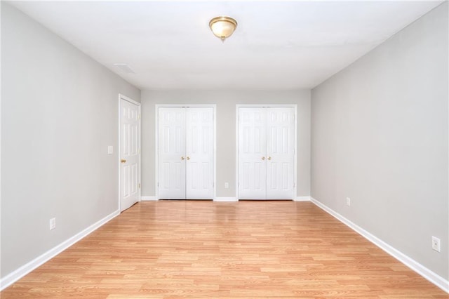 unfurnished bedroom featuring visible vents, baseboards, two closets, and light wood-style flooring