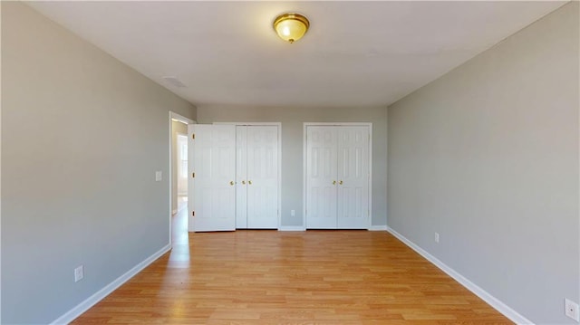 unfurnished bedroom featuring visible vents, two closets, light wood-type flooring, and baseboards