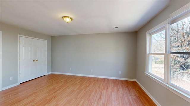 spare room featuring a healthy amount of sunlight, light wood-type flooring, and baseboards