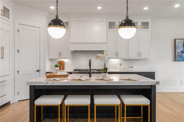 kitchen featuring white cabinetry, light stone countertops, tasteful backsplash, light hardwood / wood-style floors, and a center island with sink