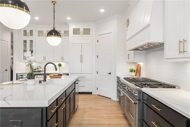 kitchen with stainless steel appliances, sink, white cabinetry, hanging light fixtures, and an island with sink