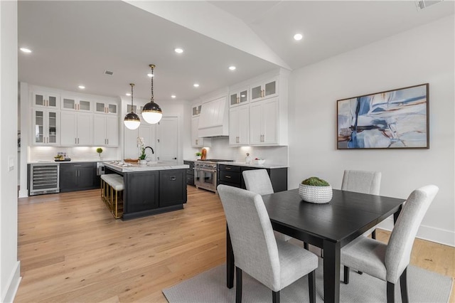 dining room featuring vaulted ceiling, light hardwood / wood-style flooring, beverage cooler, and sink